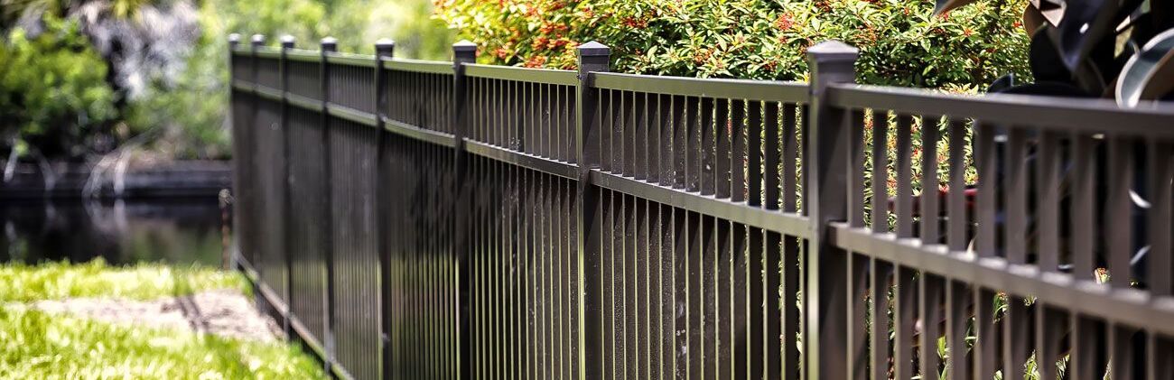 Metallzaun entlang eines Gartenwegs mit unscharfem Grün im Hintergrund.