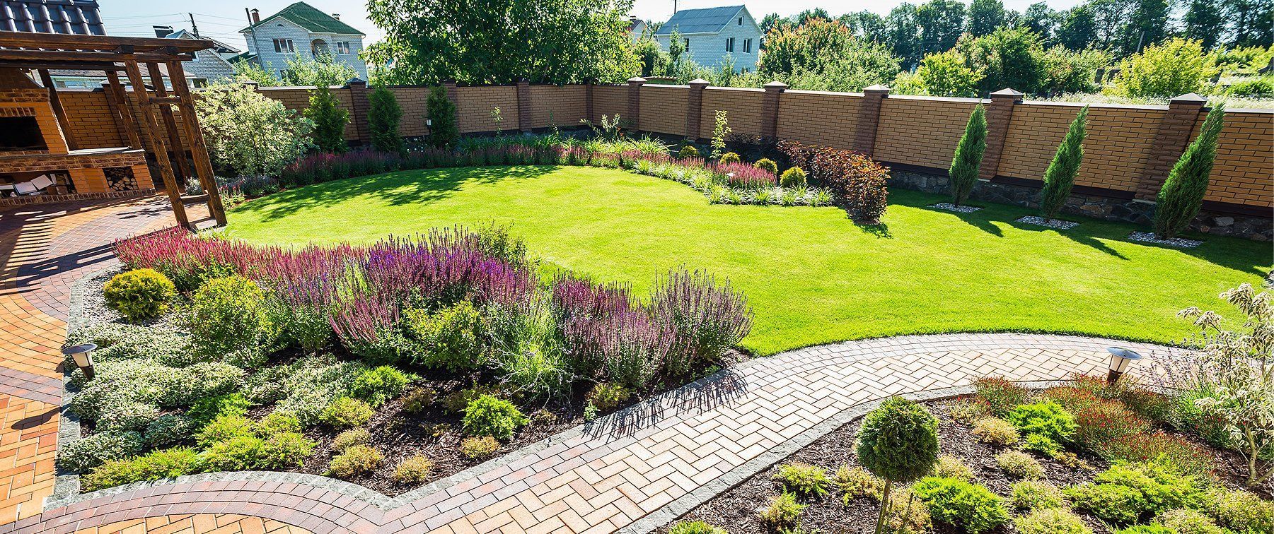 Gepflegter Garten mit üppigem grünen Rasen, Blumenbeeten und einem Ziegelzaun.